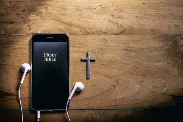The Bible app in smart phones and silver cross on a wooden table, read and listen to the voice of God, Headphone, Close up, christian concept.